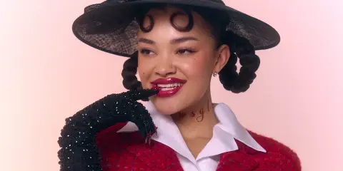 Daniela Rathana med en svart hatt och röd kavaj, med glittriga handskar och en lekfull blick.