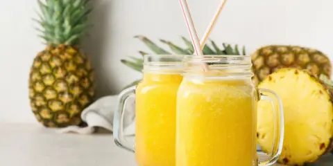 Orzeźwiający drink w ananasie, podany w słoikach, z kawałkami ananasa w tle.