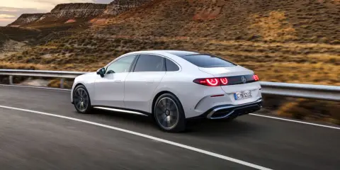 Weißer Mercedes C-Klasse EQ fährt auf einer Straße in bergiger Landschaft.