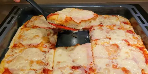 Ania gotuje pizzę. Gorąca, domowa pizza z serem i szynką, właśnie wyjęta z blachy.