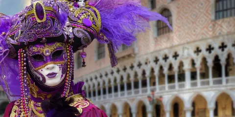 Un elaborato costume di Carnevale a Venezia, uno dei carnevali famosi in Italia, con maschera viola e oro, piume e perline.