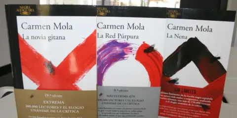 Libri di Carmen Mola: "La novia gitana", "La Red Púrpura" e "La Nena". Copertine con disegni astratti e mosche.