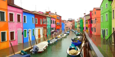 Venise : une maison colorée et d'autres maisons aux teintes vives bordent un canal où flottent des bateaux.