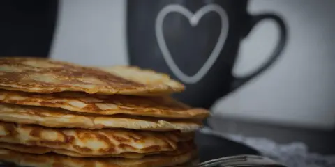 Stapel goldbrauner, **high protein pancakes** auf schwarzem Teller, daneben eine Tasse mit Herz.
