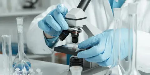 Naukowcy w niebieskich rękawiczkach analizują próbkę pod mikroskopem. To kluczowy etap w badaniach, np. przy analizie biopsji.
