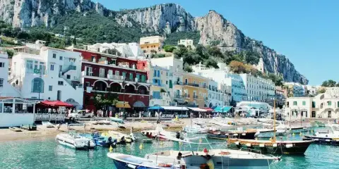 Colorate case affacciate sul mare turchese, con barche ormeggiate e montagne sullo sfondo. Un incantevole scorcio delle isole vicino Napoli.