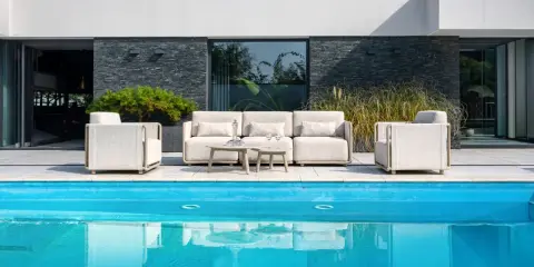 Nowoczesne meble ogrodowe z jasnej tkaniny, w tym sofa i fotele, ustawione przy basenie. Sprawdź meble ogrodowe wymiary dla tej aranżacji.