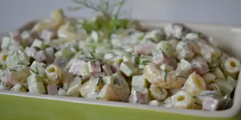 Pyszna sałatka z makaronem, szynką, ogórkiem i serem, udekorowana świeżym koperkiem.