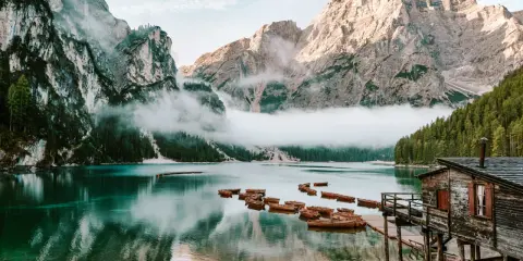 Spokojne jezioro w Dolomitach, Tyrol Włochy, z łodziami przy drewnianym molo i mgłą otulającą góry.