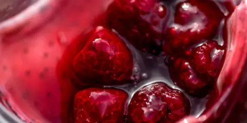 Gros plan sur des framboises dans un liquide rouge vif, parfait pour un nappage framboise facile et gourmand.