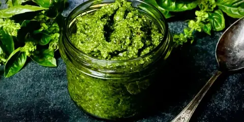 Frisches Basilikum-Pesto in einem Glas, bereit für ein köstliches basilikum pesto rezept. Daneben ein Löffel und grüne Basilikumblätter.
