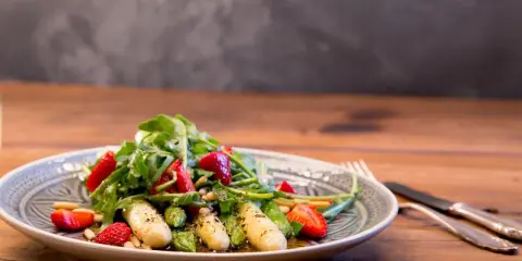 Ein frischer Spargelsalat mit Erdbeeren, Rucola und Pinienkernen, appetitlich auf einem Teller angerichtet.