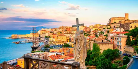 Una statua con una croce domina la vista di una città costiera colorata, perfetta per una gita fuori porta da Roma.