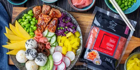 Kolorowy bowl z lososiem, ryżowymi kulkami, mango, awokado, edamame i marynowanym imbirem. Obok opakowanie różowego imbiru.