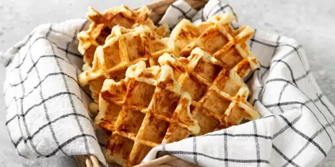 Un panier rempli de gaufres dorées, parfaites pour une recette gaufre rapide. Elles sont présentées sur une serviette à carreaux noirs et blancs.