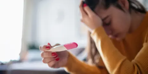 Zmartwiona kobieta trzyma test ciążowy. Czy to tokofobia, co to za lęk?