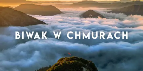 Widok z gór podczas trekkingu w Austrii. Chmury otulają szczyty, a na jednym z nich powiewa flaga.