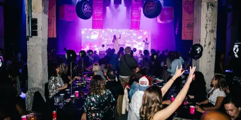 Festligt event med "Old School Brunch" i Stockholm. Människor sitter vid borden, en artist uppträder på scenen under lila ljus.