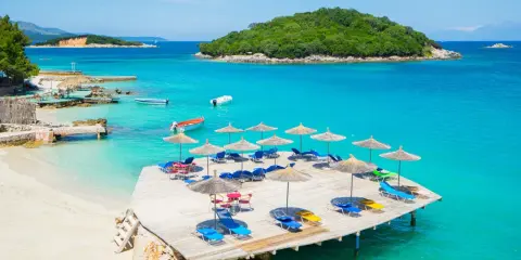 Rajskie widoki na **Albania najpiękniejsze plaże**. Turkusowa woda, piaszczysta plaża i drewniany pomost z leżakami.