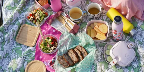 Piknikowy koc z jedzeniem: sałatki, chleb, owoce, napoje i bambuowe sztućce.