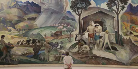 A mural depicting rural life and labor, reminiscent of the Wyeth family artists' style, with figures tending to livestock and fields under a dramatic sky.