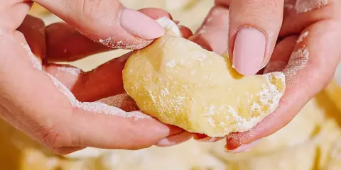 Dłonie z różowymi paznokciami lepią pierogi. Mąka lekko oprósza palce i ciasto. To idealny przepis na domowe pierogi.