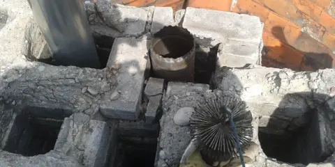 Widok na komin z widocznym metalowym czopuchem i szczotką do czyszczenia. Prawidłowe podłączenie czopucha do komina jest kluczowe dla bezpieczeństwa.