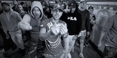 Gibbs, daj tylko czas tekst. Grupa mężczyzn w tunelu, jeden z nich w bluzie Fila, inny w bluzie z kapturem.
