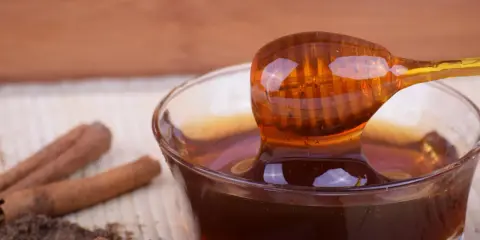 Miele di castagno, ricco di proprietà benefiche, gocciola da un cucchiaio in una ciotola. Cannella e polvere scura completano la scena.