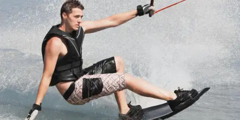 Młody mężczyzna na desce, ciągnięty przez linę, pokazuje, **wakeboarding co to** jest – sport wodny pełen adrenaliny i zabawy.
