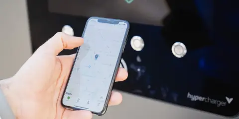 Mano che usa smartphone con mappa per trovare stazione di ricarica. L'app mostra la posizione e le opzioni per monitorare la carica.