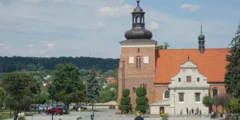 Włocławek stare miasto: plac z kościołem, wieżą i ludźmi spacerującymi w słoneczny dzień.