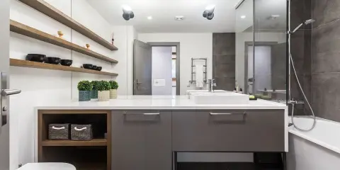 Moderno baño con ducha, bañera y lavabo sobre mueble gris. Estanterías de madera con cuencos negros. Un ejemplo de presupuesto de reforma de baño.