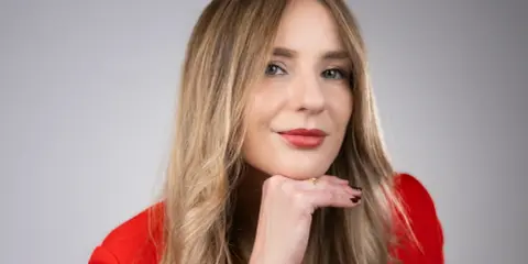 Francesca Florio, con un blazer rosso, appoggia il mento sulla mano, un sorriso pensieroso.