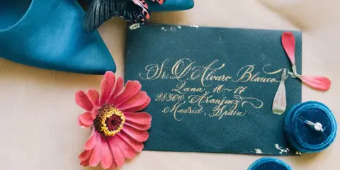 Elegancka koperta z zaproszeniem na wesele, pierścionek zaręczynowy i kwiaty. Warto wysłać je z wyprzedzeniem, by goście mogli się przygotować.