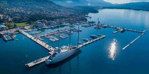 Ein riesiges Segelschiff liegt im porto hafen, umgeben von vielen Yachten und einer Stadt am Fuße von Bergen.
