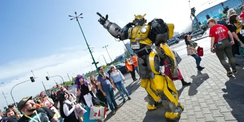 Bumblebee wita fanów na Pyrkonie. Tłum ludzi w kostiumach i z torbami idzie chodnikiem.