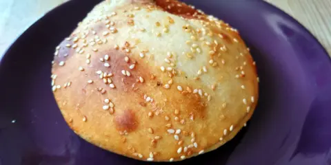 Bułka do hamburgerów posypana sezamem na fioletowym talerzu.