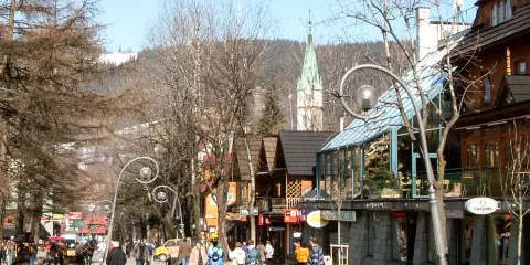Spacer po urokliwej ulicy Krupówki w Zakopanem. Ludzie przechadzają się, podziwiając góralską architekturę i widok na Tatry.