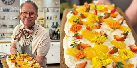 En glad man håller upp en vacker påsktårta i långpanna, dekorerad med grädde, jordgubbar, aprikoser och gula blommor.