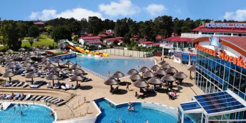 Słoneczny aquapark nad morzem z basenami, zjeżdżalniami i leżakami pod parasolami.