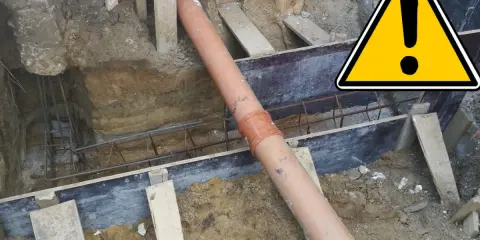 Budowa domu: widoczna rura kanalizacyjna w wykopie, zbrojenie i elementy szalunku.