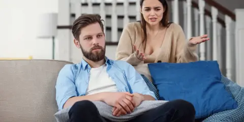 Mężczyzna siedzi zamyślony, podczas gdy kobieta z wyrzutem gestykuluje. Scena sugeruje porzucenie żony w chorobie, gdy on wydaje się obojętny.