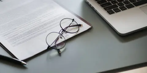 Okulary na dokumencie z tekstem, obok laptopa. Dokument może zawierać pełnomocnictwo lub strategię marketingową.