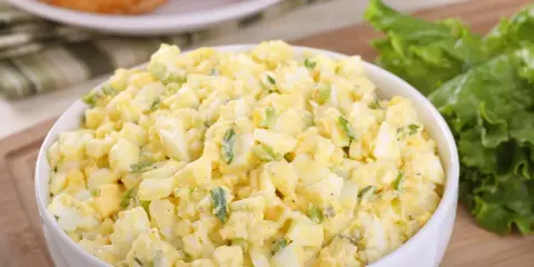 Pyszna sałatka z jajkiem, idealna na śniadanie lub lunch. Podana w białej misce, obok świeżych liści sałaty i chrupiących croissantów.