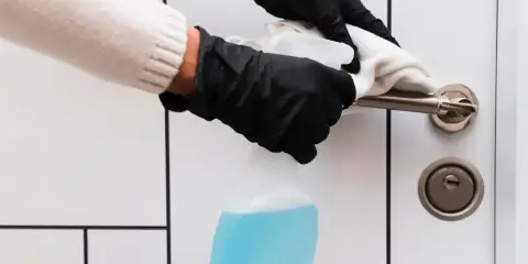 Ręce w czarnych rękawiczkach czyszczą klamkę drzwi białą ściereczką i płynem. Dowiedz się, czym wyczyścić zżółknięte drzwi.