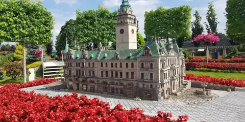 Miniatura ratusza z wieżą zegarową, otoczona czerwonymi kwiatami. Jedna z wielu atrakcji Kotliny Kłodzkiej.