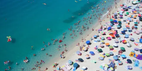 Spiaggia affollata con ombrelloni colorati e bagnanti nell'acqua cristallina, un'immagine perfetta per scoprire le località di mare più economiche in Italia.