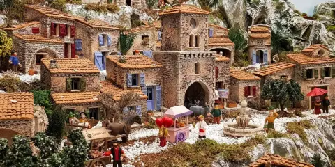 Une **crèche provençale** animée avec des santons, des maisons en pierre, un âne, un chariot et une fontaine, le tout dans un paysage rocheux.