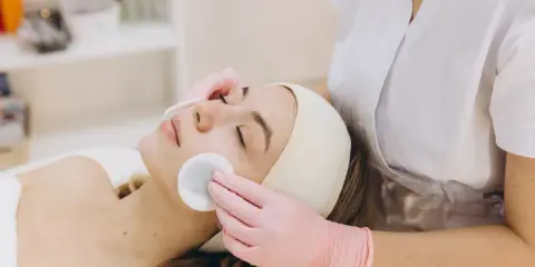 Una donna riceve una pulizia del viso con dischetti di cotone. La durata di una pulizia del viso varia, ma questo momento di relax è prezioso.